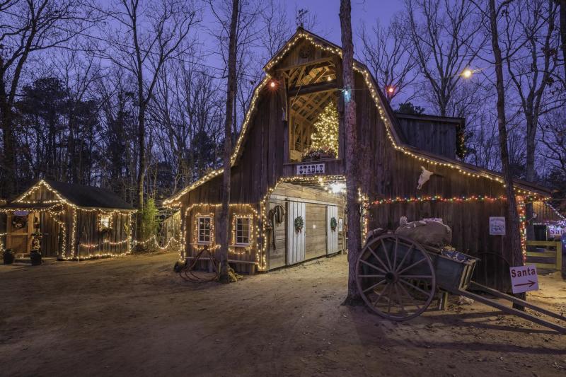 Rustic barn at Sweet Valley Ranch decorated with strings of glowing Christmas lights and a lit tree inside, creating a warm holiday glow against the evening sky in Fayetteville, North Carolina.
