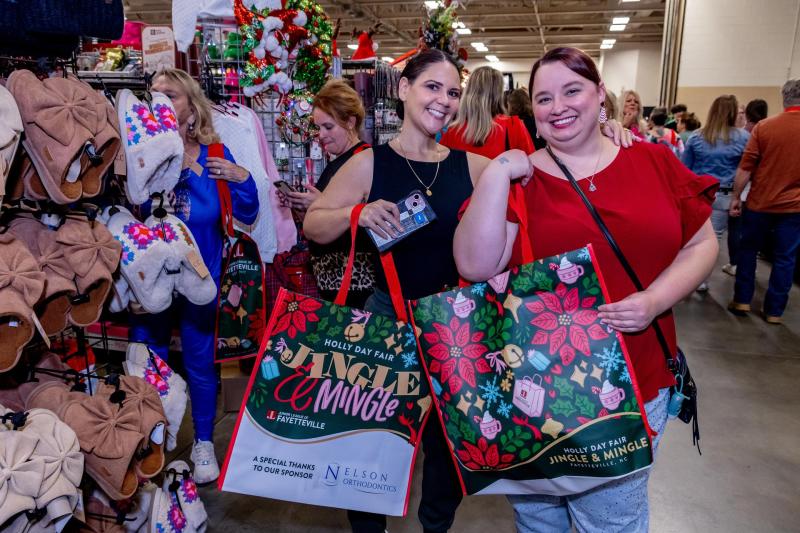 Shoppers smile and hold festive tote bags while browsing booths of holiday gifts and handmade crafts at the Holly Day Fair inside the Crown Expo Center in Fayetteville, NC.