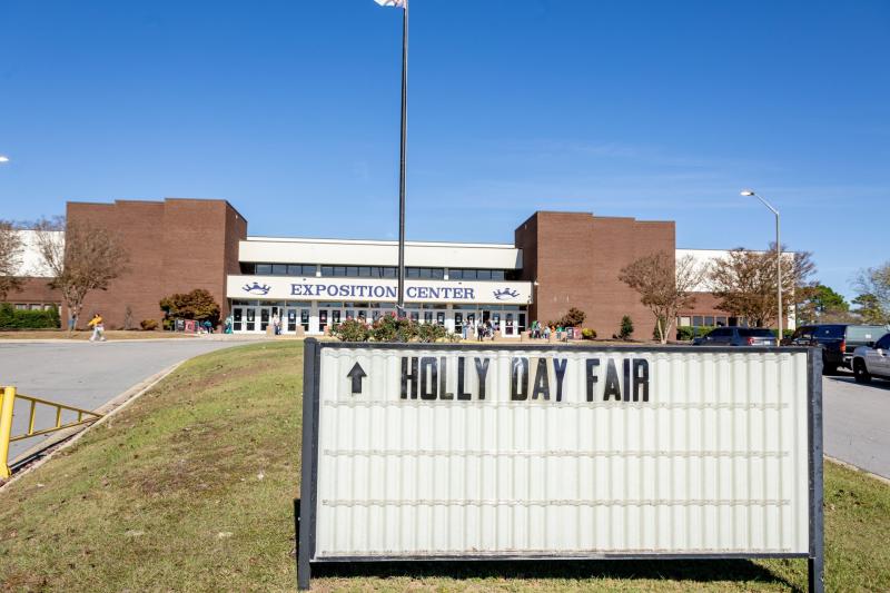 A sign reading “Holly Day Fair” points toward the entrance of the Crown Expo Center in Fayetteville, NC, where visitors arrive for the annual holiday shopping event.