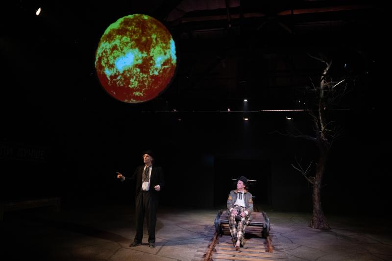 A performance at Bas Bleu with a person sitting on railroad tracks with a sun being projected on the wall behind them