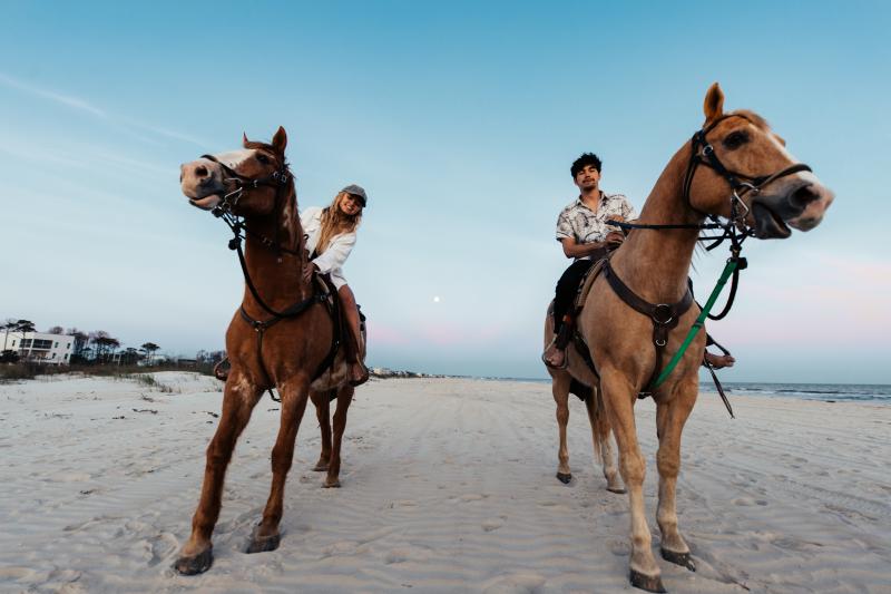man and woman, each on horseback on the beach
