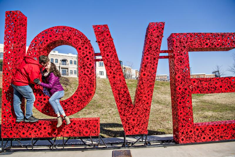 Oversized LOVE metal art in red with couple kissing standing in front of the artpiece
