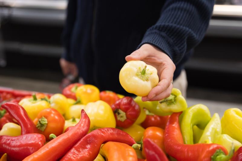 Shopper holding farm-grown produce above a colourful display of peppers at Don-O-Ray Farm Market in Kelowna.