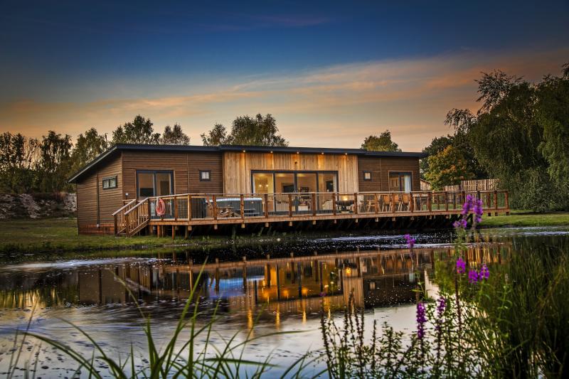 A woodlen lodge lit by warm lights, behind a lake.
