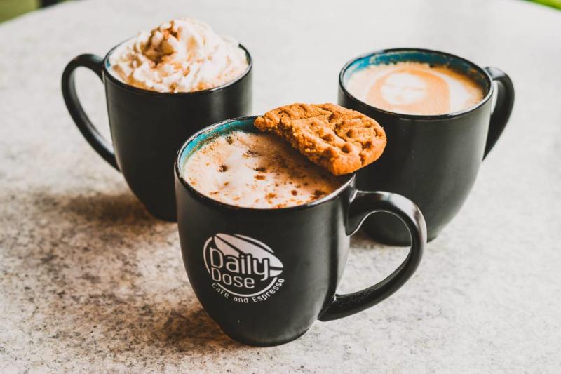 Three full coffee cups, one topped with a half cookie from Daily Dose