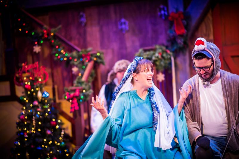 A woman dressed in a blue dress with a blue and white head scarf on stage talking to a man wearing a sock monkey hat