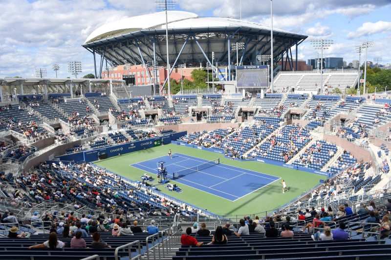 Arthur Ashe Stadium at the US Open with a packed daytime crowd and blue courts