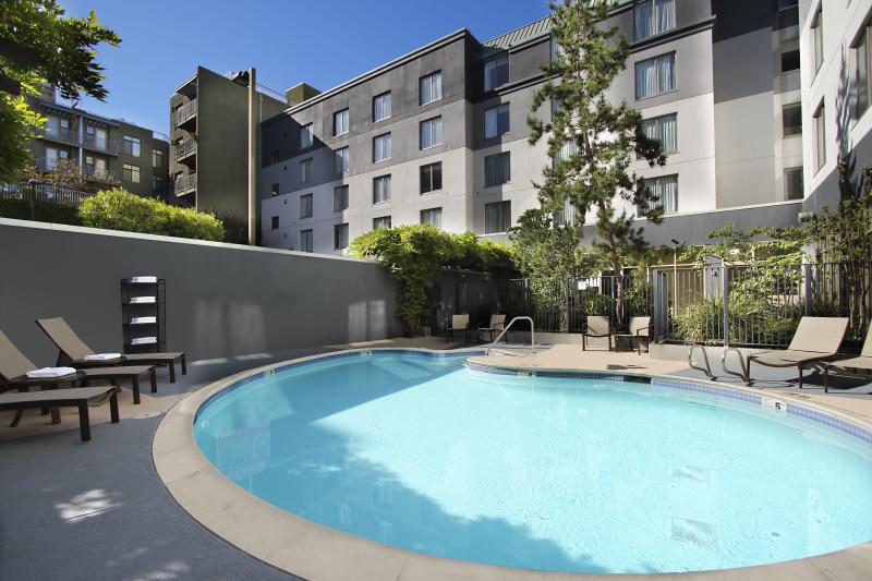The peacefully secluded pool at the Courtyard Oakland Downtown Hotel surrounded by lounge chairs and greenery.