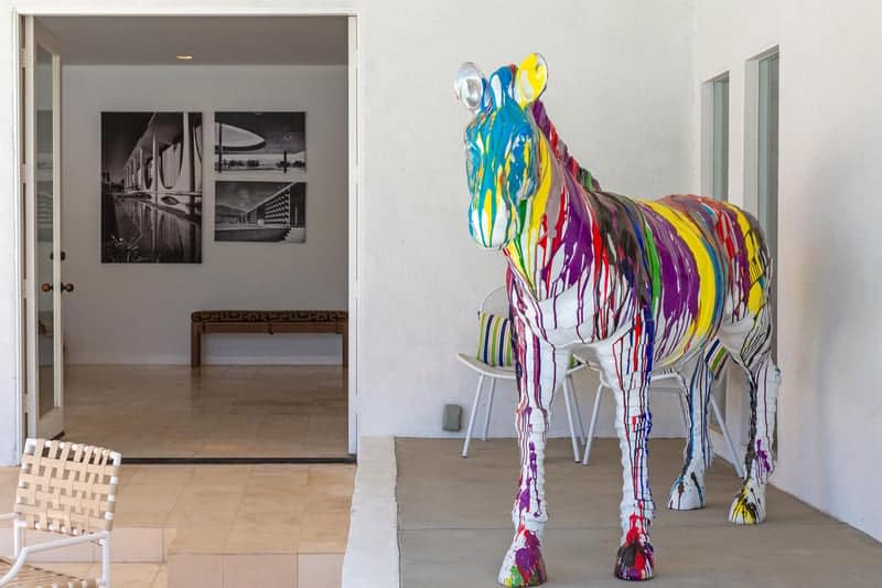 A vibrantly painted horse sculpture placed in the patio of a contemporary house with minimalist furniture and black and white wall art in the background.