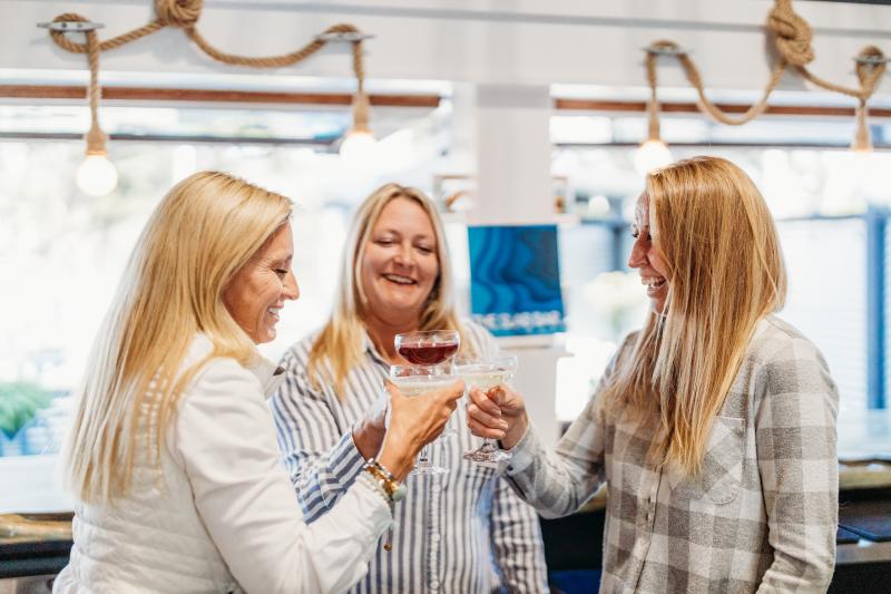 Partners Mishelle Westendorf, Lucy Gillies, and Tanya Slye hold up their drinks.