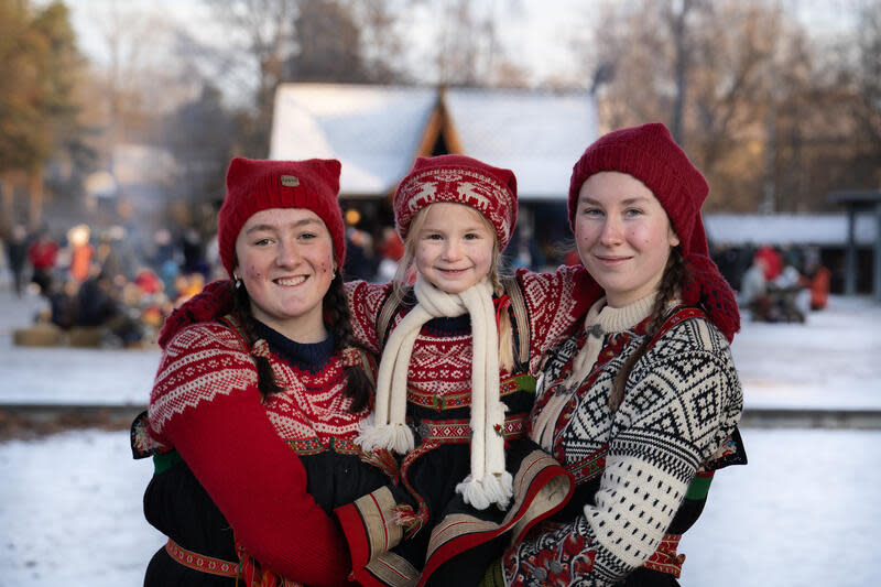 A small child between two young women in traditional Norwegian costume at the Norsk Folkemuseum's Christmas fair