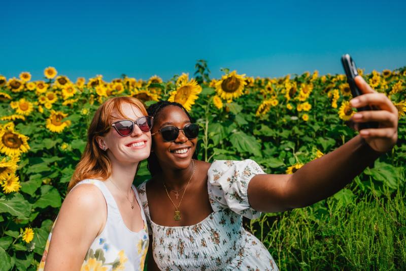 Two girls taking a selfie in a sunflower field.