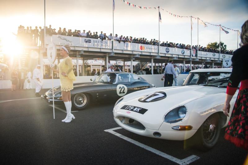 Two cars on the start line at the vintage car festival with crowds in pit lane and grandstand, Goodwood Revival