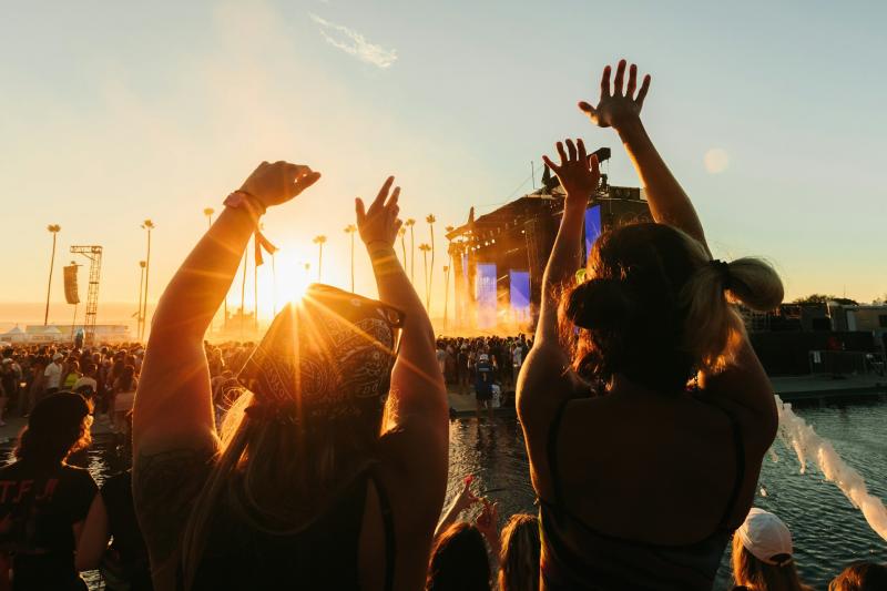 two people silhouetted with their arms up at a festival, the stage is in the distance