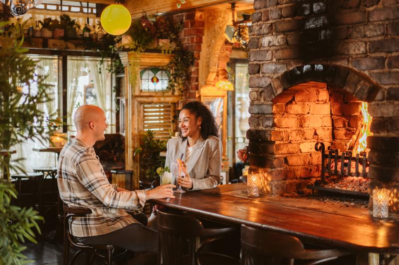 Young couple enjoying a drink by the fire at Gin and Juice