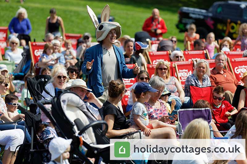 A man in a rabbit headdress in the audience at outdoor theatre.