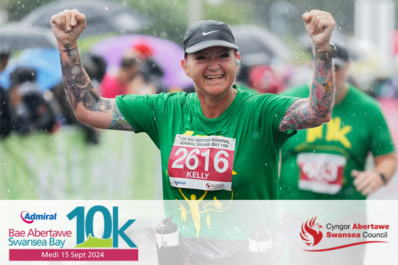 A female runner at the 10k holding her arms aloft and smiling.