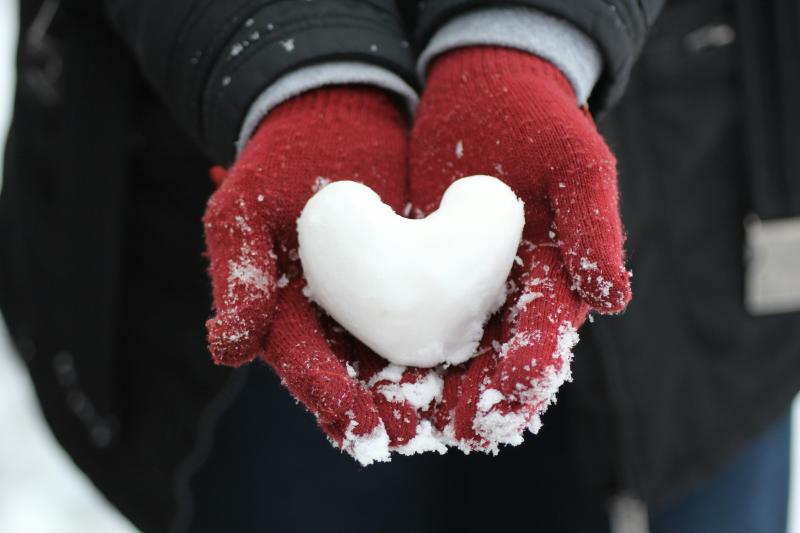 A person with red gloves holding a piece of snow shaped like a heart in their palms.