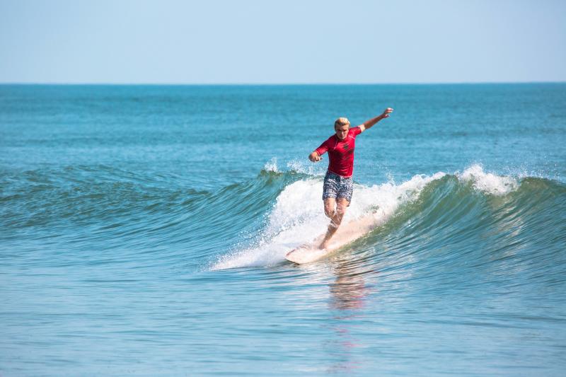 surfer riding the line of a wave in blue water wearing a red competitive jersey