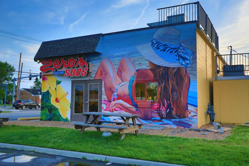 Artist Eric Lindberg of TALENT MuralsVirginia Beach, VAWomen reclining on the beach. The property owner and artist worked together on ideas that kept with the beachy vibe of the other murals at the restaurant. The artist used his hyper realism style on a women reclining at the beach and inserted tropical hibiscus flowers on the left side of the building.