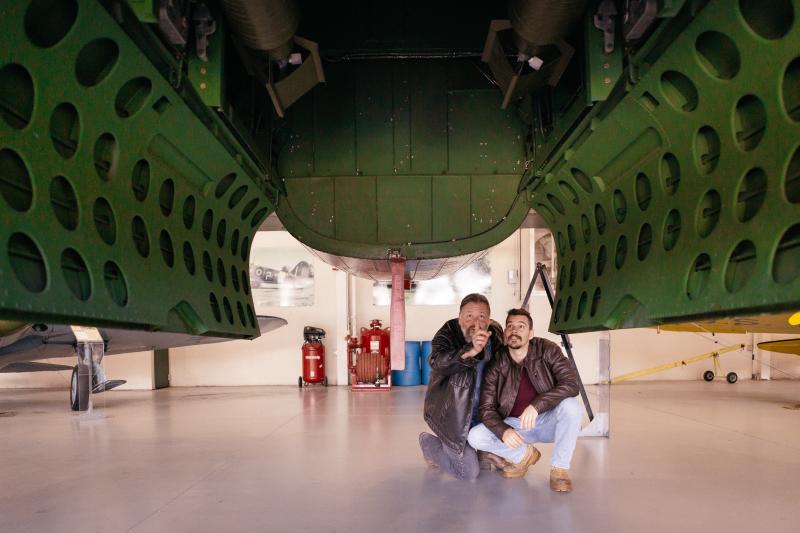 two men crouched under a plane at an aviation museum