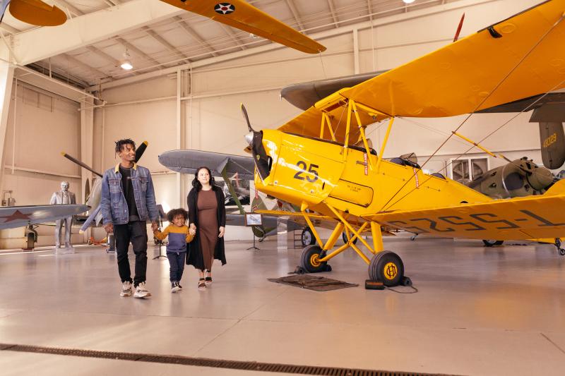 man, woman and small boy walking by a yellow plane in a museum