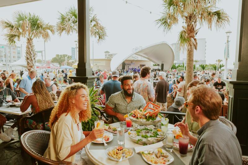 Adults dining with friends at Virginia Beach Oceanfront in front of King Neptune