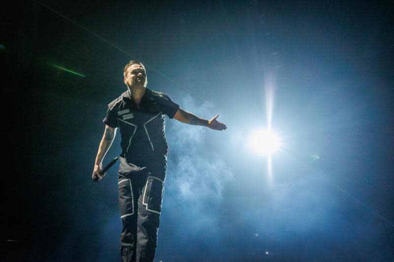 The lead singer of Shinedown performs on stage during a concert in front of a bright spotlight.