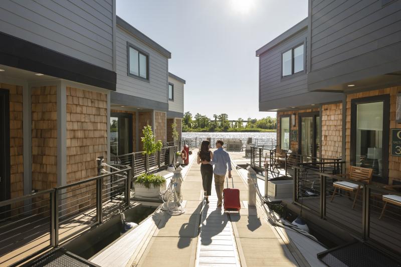 couple walking toward their houseboat vacation rental with their suitcase by the river.