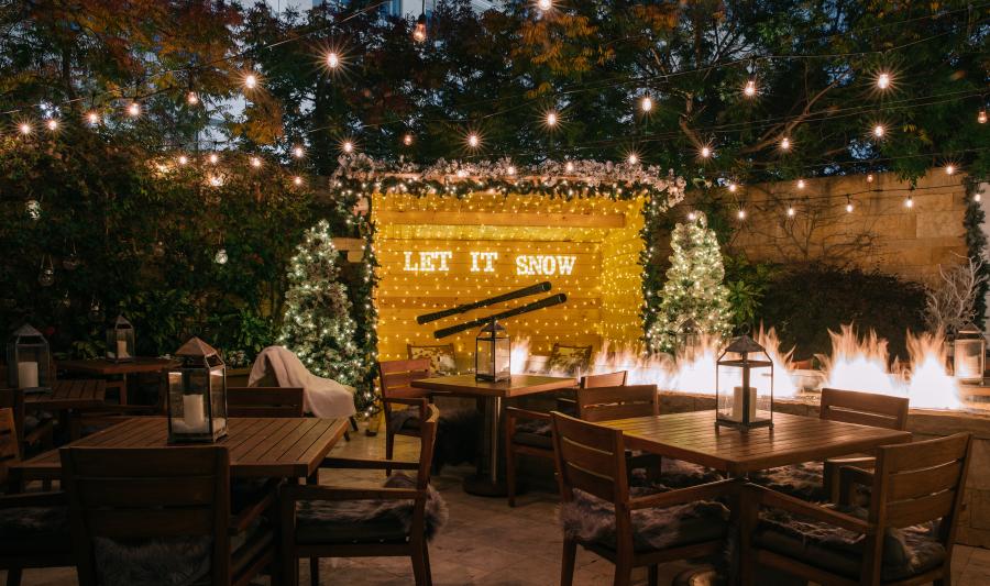 Tables set under twinkling lights with a fireplace and festive decorations at Après Village.