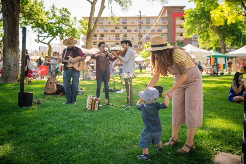 A woman holds the hands of a young child as they dance to a live band at the Downtown Growers Market