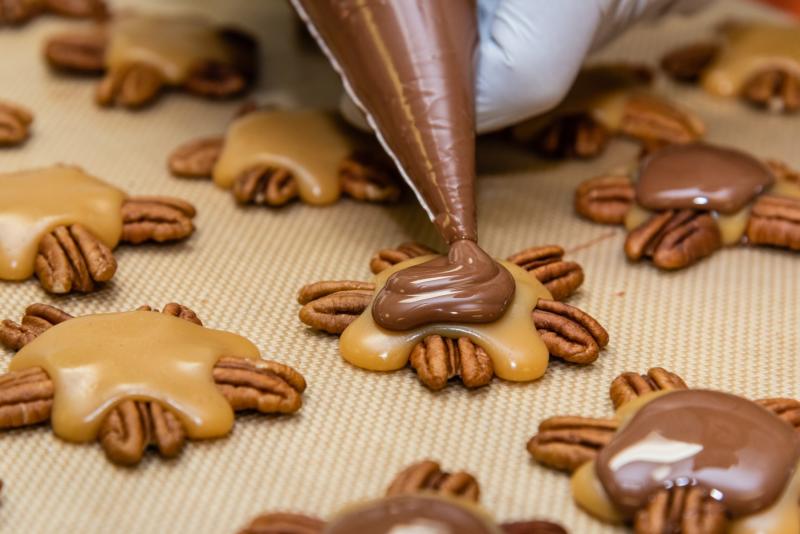 Someone pipes chocolate on pecan caramel candies at Elixir Boutique Chocolates