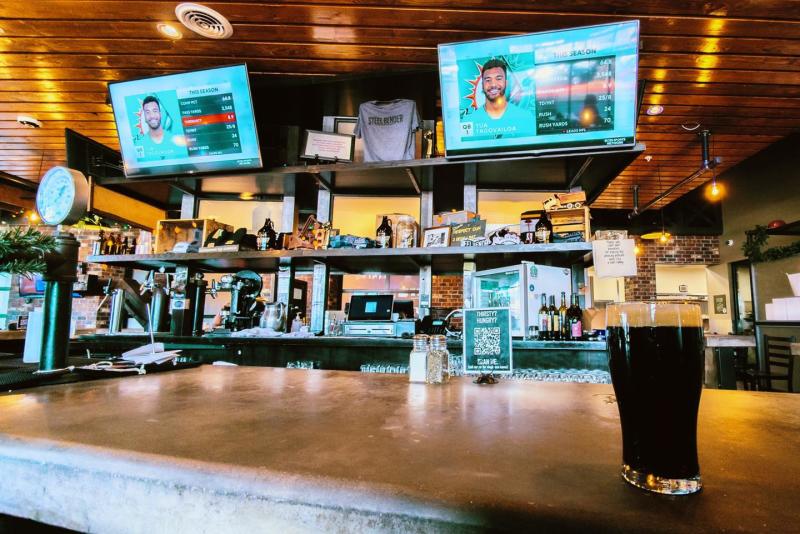 A beer sits on the counter at Steel Bender Brewyard. In the background two TVs play an NFL game