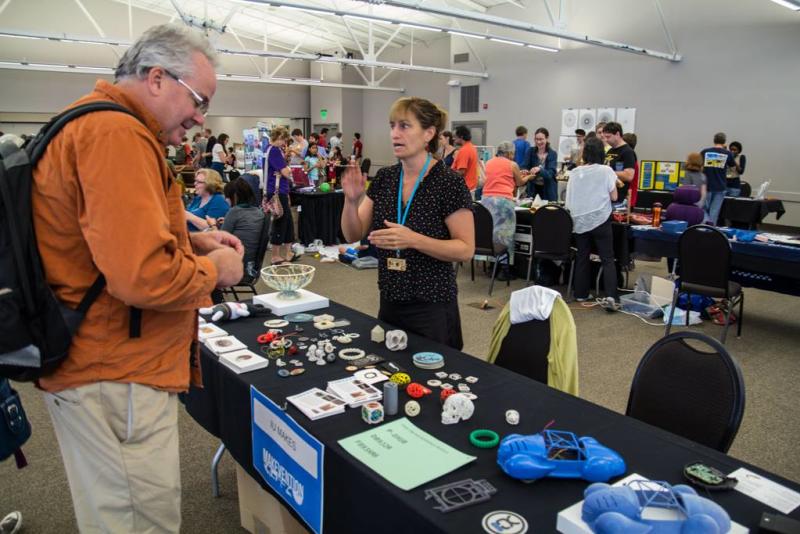 People talking at a booth at Makevention