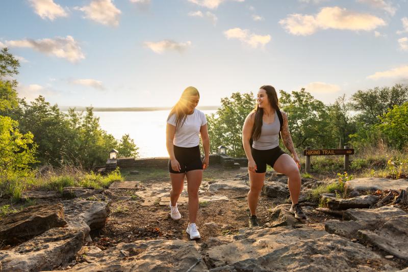 Two women hiking at Lake Brownwood State Park. The view of the water on the horizon is in the background.