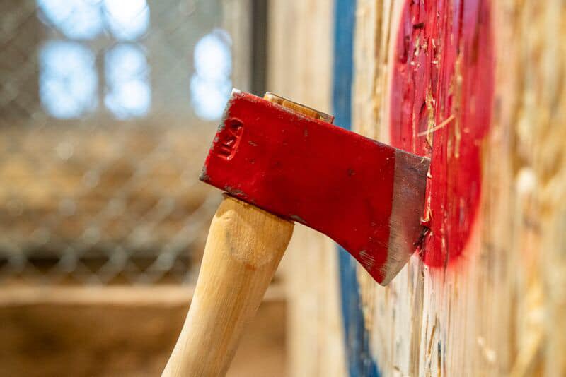 Image is of an axe that is embedded in a wood bullseye.