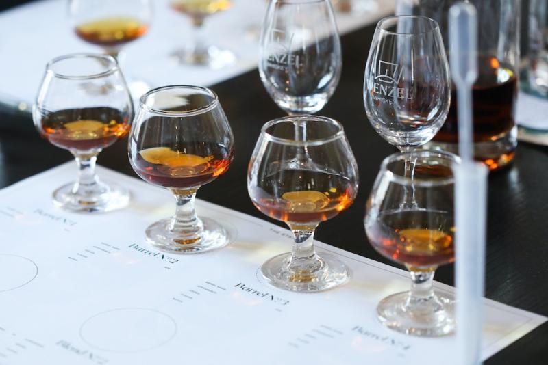 Four bourbon glasses sit on a white placemat next to a small pipette and test tube people can use to make custom blends