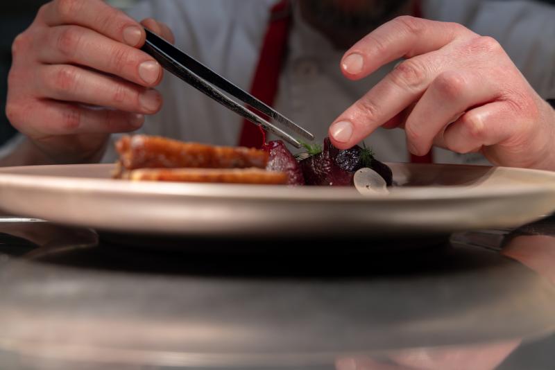Chef Using Tweezers to Plate a Dish with Precision on a Plate
