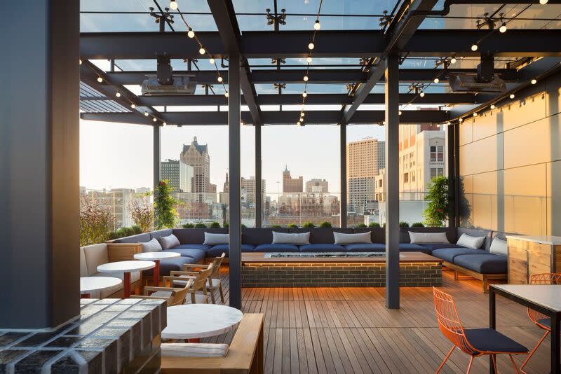 Modern rooftop lounge at The Outsider in Milwaukee with cushioned seating, wooden floors, string lights, and skyline views through a glass roof.