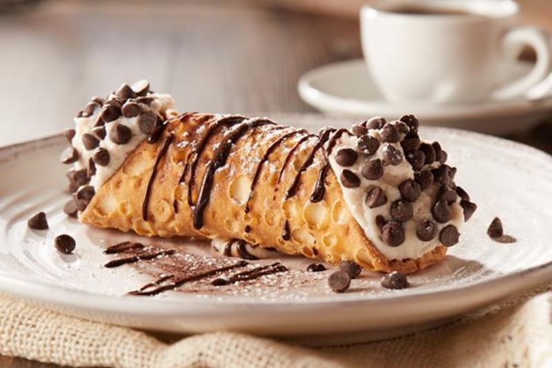 A large cannoli overloaded with filling and chocolate chips, drizzled with chocolate and dusted with sugar from Buca di Beppo