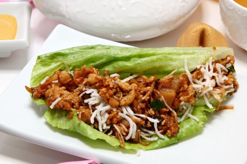 A white plate with a lettuce wrap loaded with chicken and thin-sliced vegetables from PF Changs