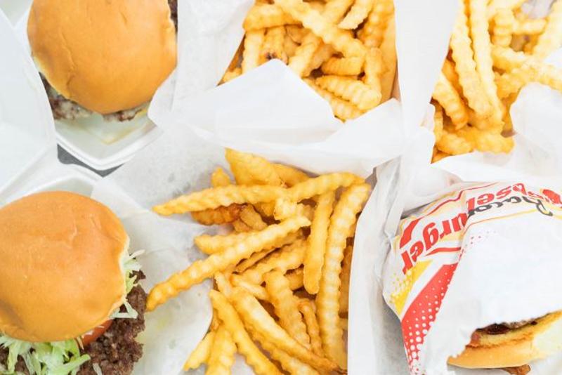 Four burgers and two orders of French fries on white paper plates from Wagner's Drive-In