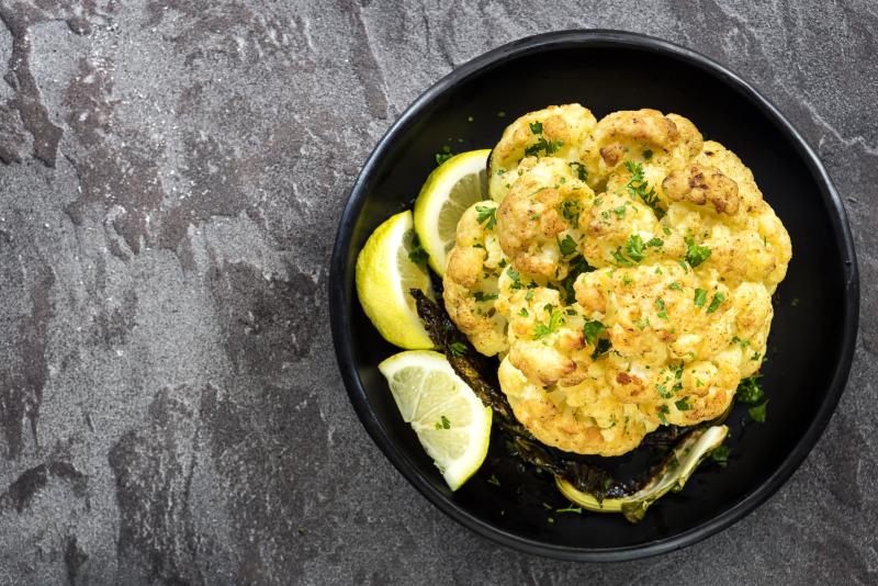 Roasted whole cauliflower with lemon, in black serving dish, top view.