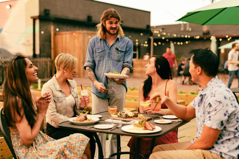 Four friends dining outside on patio waiter delivering food