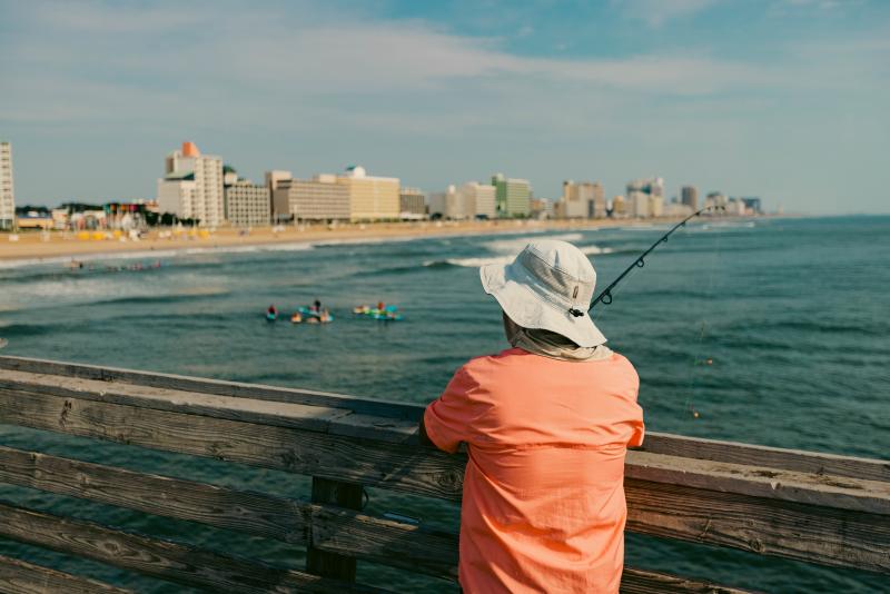 person standing with fishing rod leaning on pier