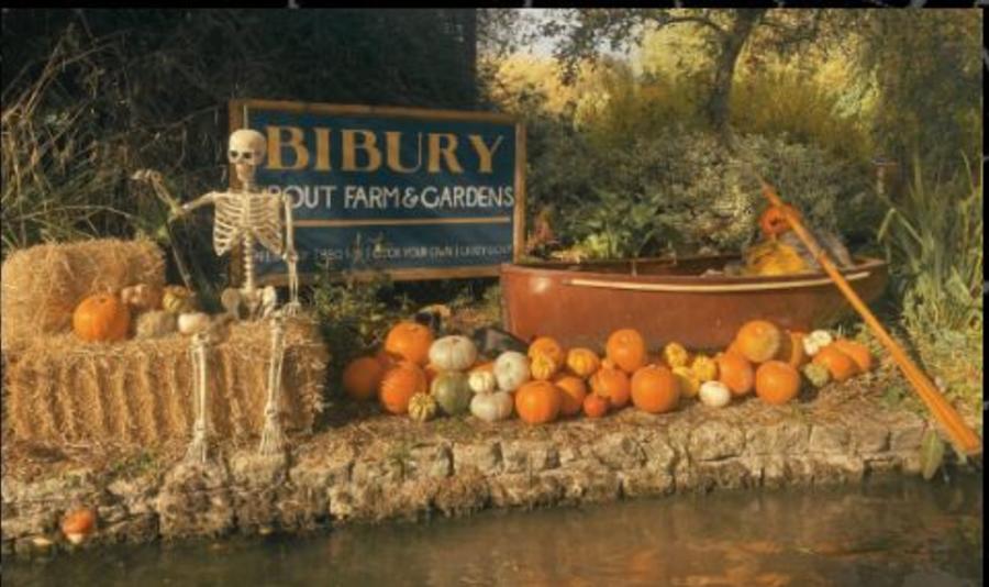 Autumn display of pumpkins, hay bales and a skeleton beside a pond at Bibury Trout Farm in the Cotswolds.