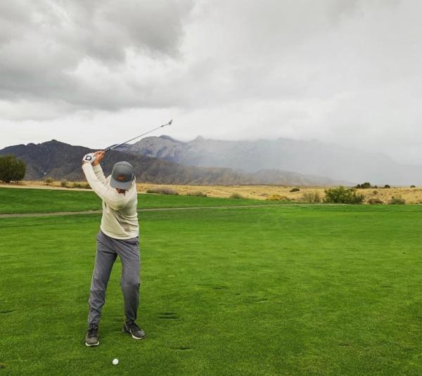 A man is mid-swing, about to hit a golf ball, at Sandia Golf Club