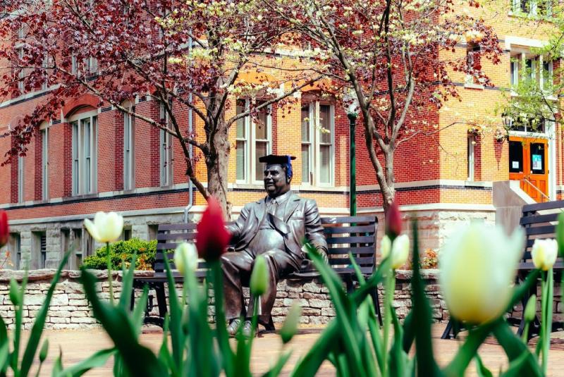 The Herman B Wells statue wearing a graduation cap on a spring day
