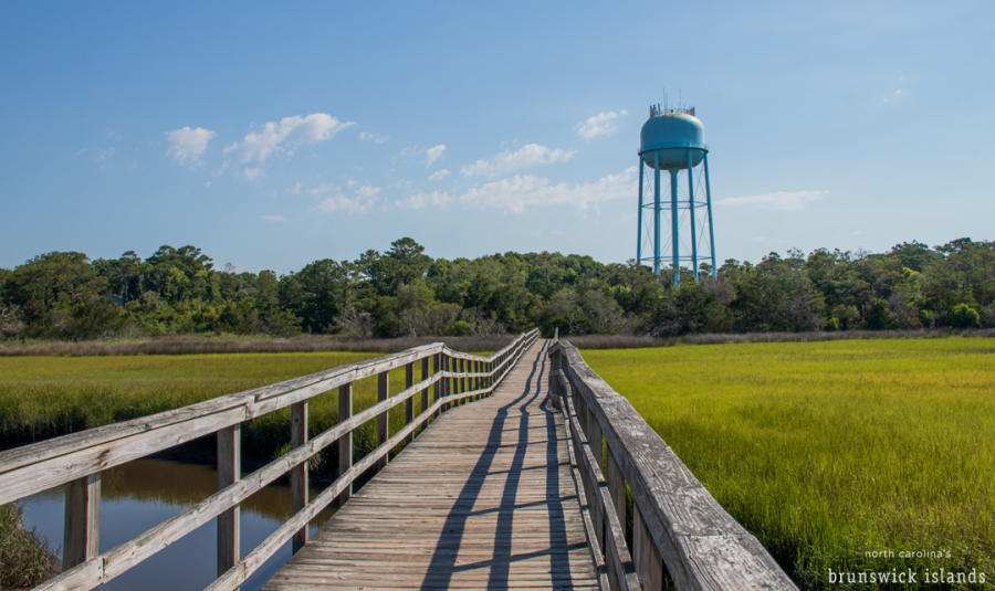 a wooden walkway extending over the marsh on Oak Island with a blue water tower in the distance