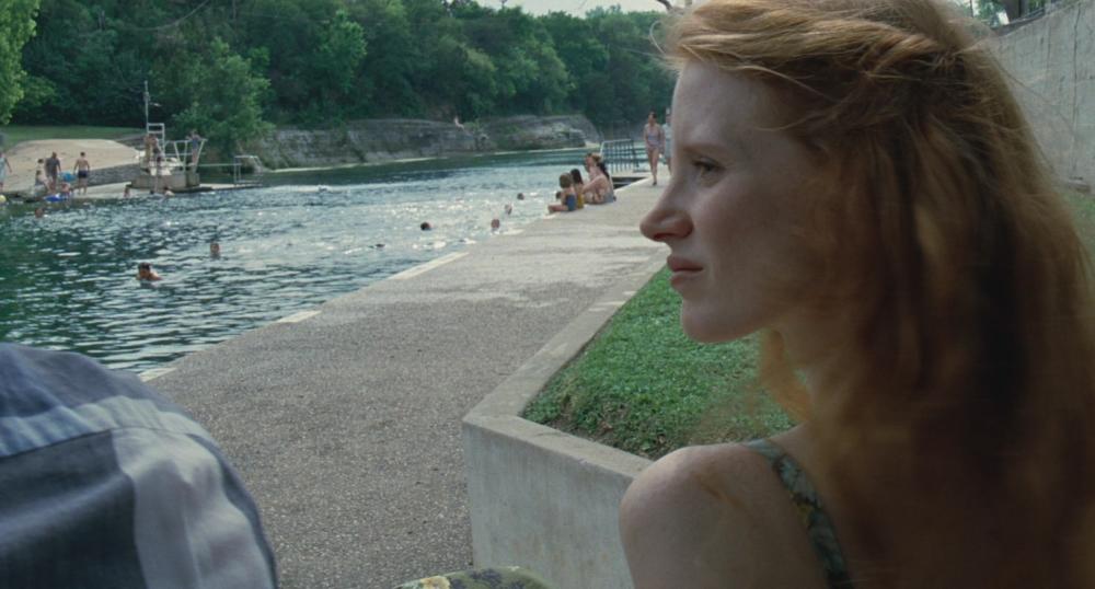 Tree of Life Screengrab, showing Jessica Chastain looking to the side of the frame. Behind her, people are swimming in Barton Springs Pool